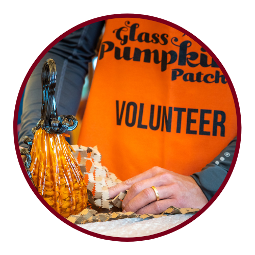 Volunteer holding glass pumpkin in orange apron with volunteer text.